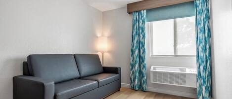 Una sala de estar moderna con un sofá gris oscuro, una lámpara de pie y una ventana con cortinas azules.
