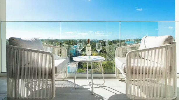 Un balcon avec des fauteuils en osier et une table, une bouteille de vin et un verre.