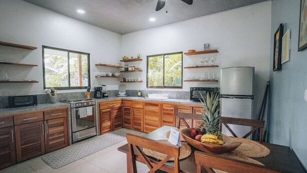 A modern kitchen with wooden cabinets, a stove, a refrigerator, and a dining area with a table and chairs. - Mahali 2: House with 2 bedrooms in Puerto Viejo (Puerto Viejo de Talamanca)
