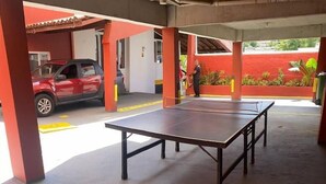 A covered outdoor area with a ping pong table, a red car, and a person standing near a door. - Point PRV (Salvador)