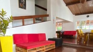 A spacious living area with a wooden floor, a red sofa, a yellow planter, and a dining area with wooden chairs. - Point PRV (Salvador)