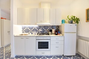 Une cuisine de taille réduite, avec des meubles blancs, une cuisinière à gaz, un four et un réfrigérateur.
