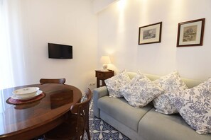 Un salon comprenant un canapé, un téléviseur fixé au mur, une table à manger avec des chaises et une lampe.
