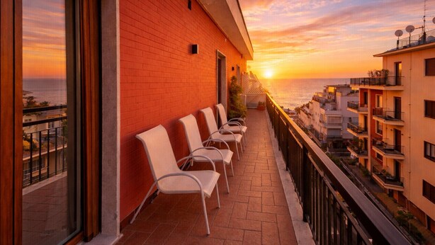 A balcony with white chairs, a red brick wall, and a view of the sunset over the sea. - AMORE RENTALS - Casa Clara with Air Conditioning and Balcony (Sorrento)