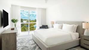 Ein modernes Hotelzimmer mit einem großen Bett, einem Deckenventilator, einem Fernseher, einem Nachttisch und Blick ins Freie.