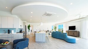 Een modern interieur met een keuken, eetruimte en woonkamer, met een centraal eiland, blauwe zitplaatsen en een flatscreen-tv.
