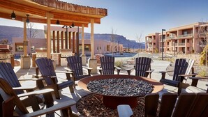 An outdoor seating area with Adirondack chairs and a fire pit, surrounded by a wooden pergola and a view of a mountain. - Moab | Desert Basecamp Retreat | Pool + Hot Tub | 2BR (Moab)
