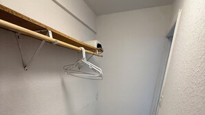 En smal hall med en hylla i trä, ett hängande metallställ och ett golv med marmorliknande mönster.