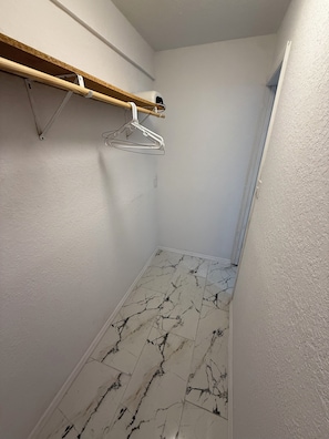 Ein schmaler Flur mit Holzregal, einem hängenden Metallgestell und einem Boden mit Marmoroptik.