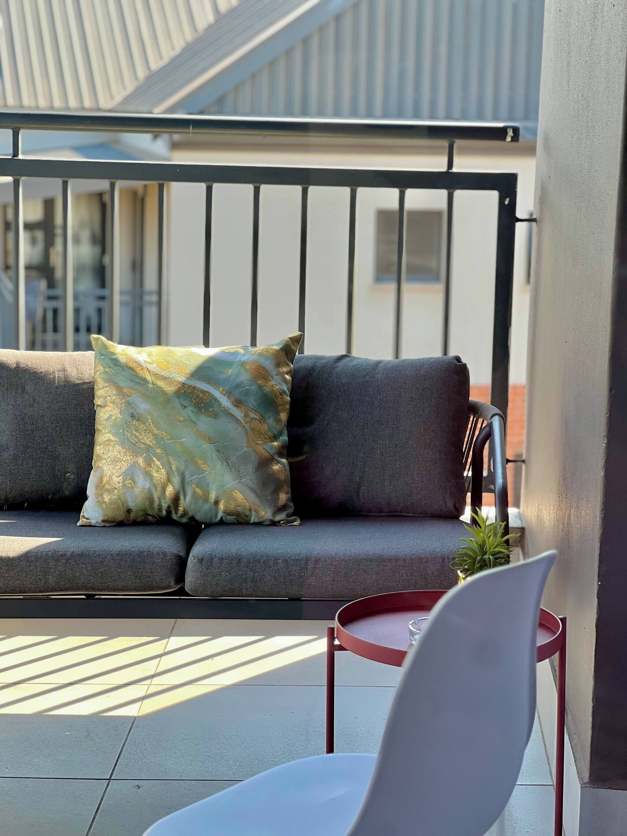 A balcony with a grey sofa, a decorative pillow, a small potted plant, and a red chair.