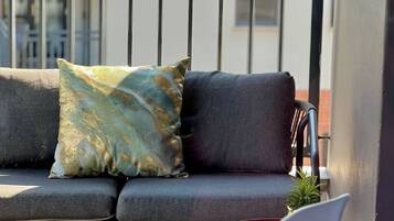A balcony with a grey sofa, a decorative pillow, a small potted plant, and a red chair.