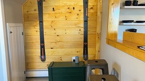 Ein Zimmer mit Holzwänden, zwei Ski, eine grüne Aufbewahrungsbox und ein Metallhocker.