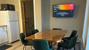 Ein Konferenzraum mit einem Holztisch, vier grünen Stühlen, einem an der Wand montierten Flachbildfernseher, einer Mikrowelle und einem Kühlschrank.