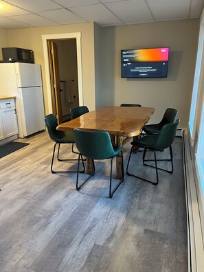 A conference room with a wooden table, four green chairs, a flat-screen TV mounted on the wall, a microwave, and a refrigerator. - Cozy Trailside Getaway. Snowmobile and ATV Trail Access. Near Sugarloaf. (Eustis)
