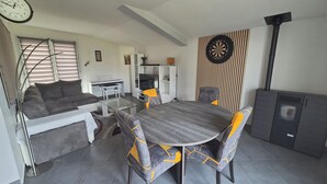 Ein gemütlicher Wohnbereich mit Esstisch, Stühlen, einer Couch, einem Fernseher, einer Dartscheibe und einem Kaminofen.