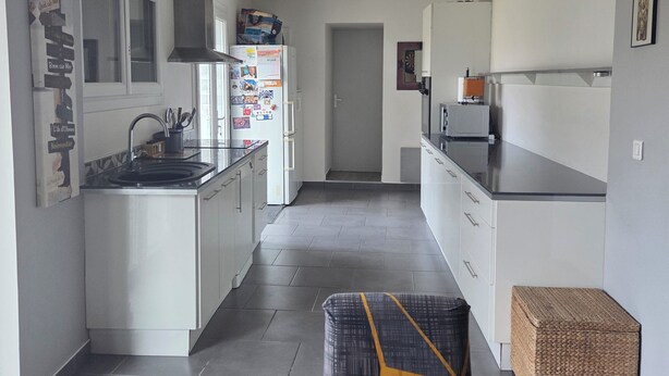 Eine moderne Küche mit weißen Schränken, einer zentralen Kochinsel und einem Essbereich mit einer grauen Couch.
