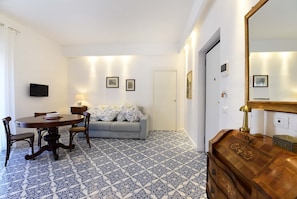 A room with a round dining table, a sofa, a TV mounted on the wall, and a patterned floor. - Casa Clara in Sorrento (Sorrento)