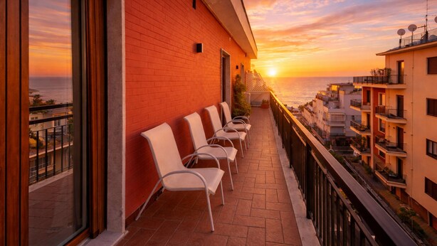 A balcony with chairs, a red brick wall, and a view of the sunset over the sea. - Casa Clara in Sorrento (Sorrento)