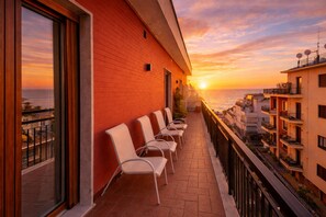 Een balkon met stoelen, een rode bakstenen muur en uitzicht op de ondergaande zon boven de zee.