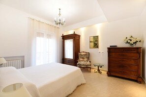Un dormitorio con cama, cómoda, silla, una mesita y una araña.