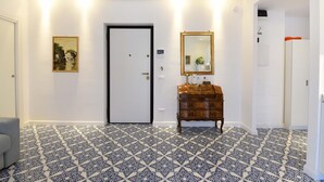 A hallway with patterned flooring, a door, a dresser, a mirror, and a framed picture on the wall. - Casa Clara in Sorrento (Sorrento)