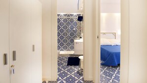 A narrow hallway leading to a bathroom with patterned tiles and a bed with a blue bedspread. - Casa Clara in Sorrento (Sorrento)