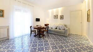 A room with a dining table, chairs, a sofa, a TV, and patterned floor tiles. - Casa Clara in Sorrento (Sorrento)