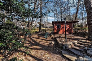 A red wooden structure in a wooded area with a stone pathway leading to it.