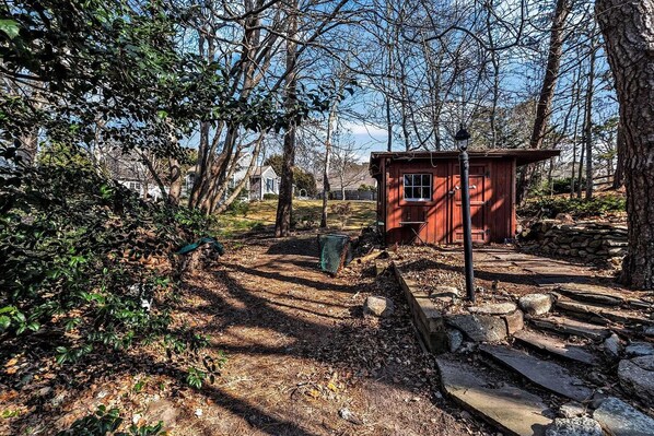 Une structure en bois rouge, située dans une zone boisée, et un sentier en pierre qui y mène.