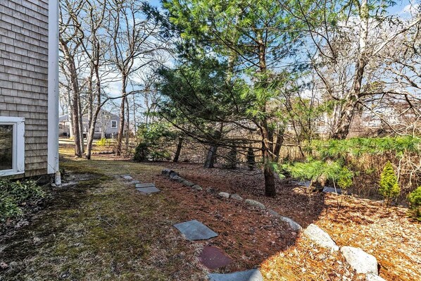 A residential backyard with a stone pathway, trees, and a house.