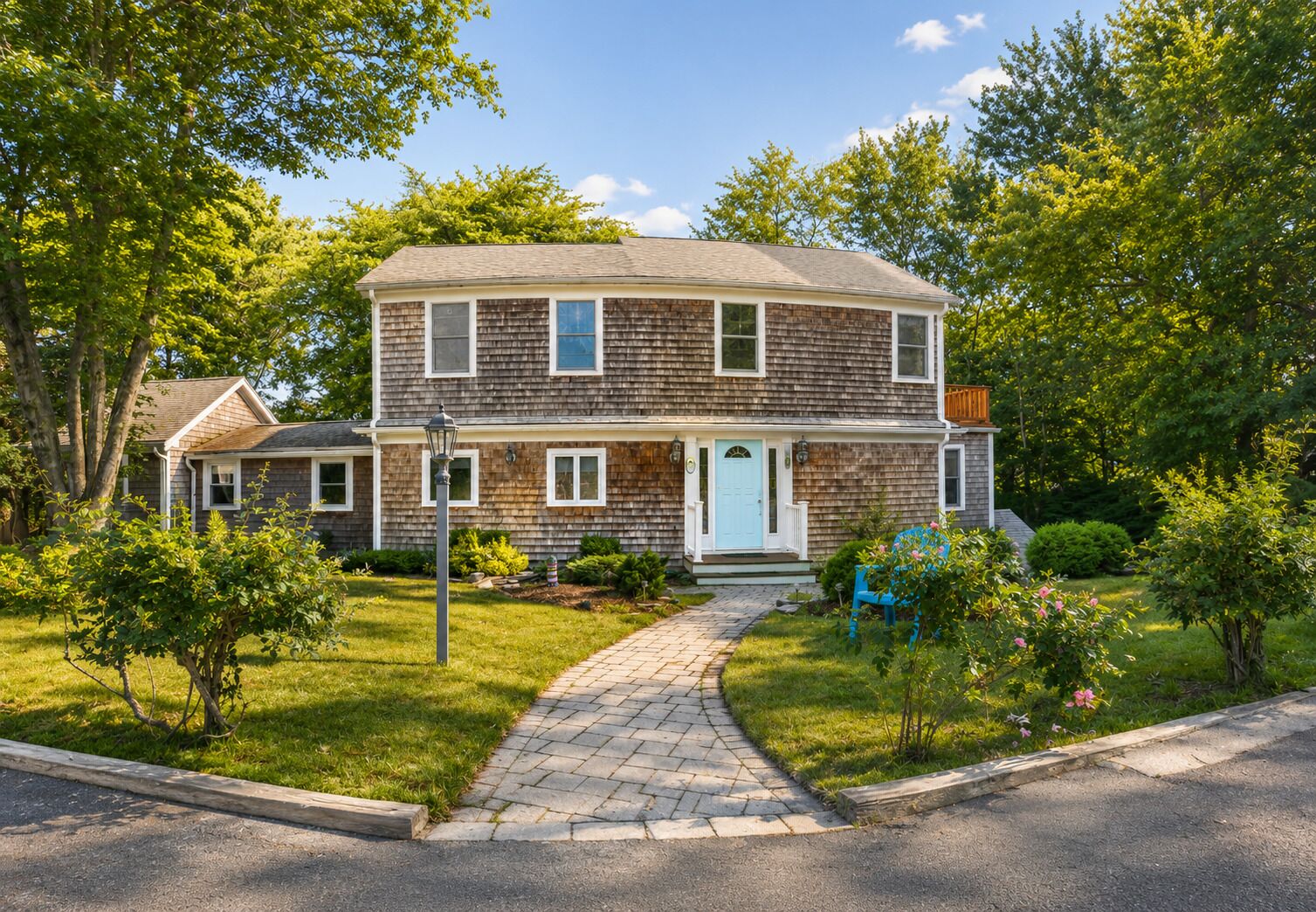 A two-story house with a front porch, a pathway leading to the door, and a small garden with bushes and flowers.