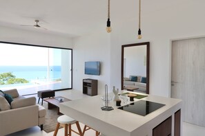 Ein modernes Wohnzimmer mit einem großen Fenster, einem Deckenventilator, einem Flachbildfernseher und einem Essbereich mit Barhocker.