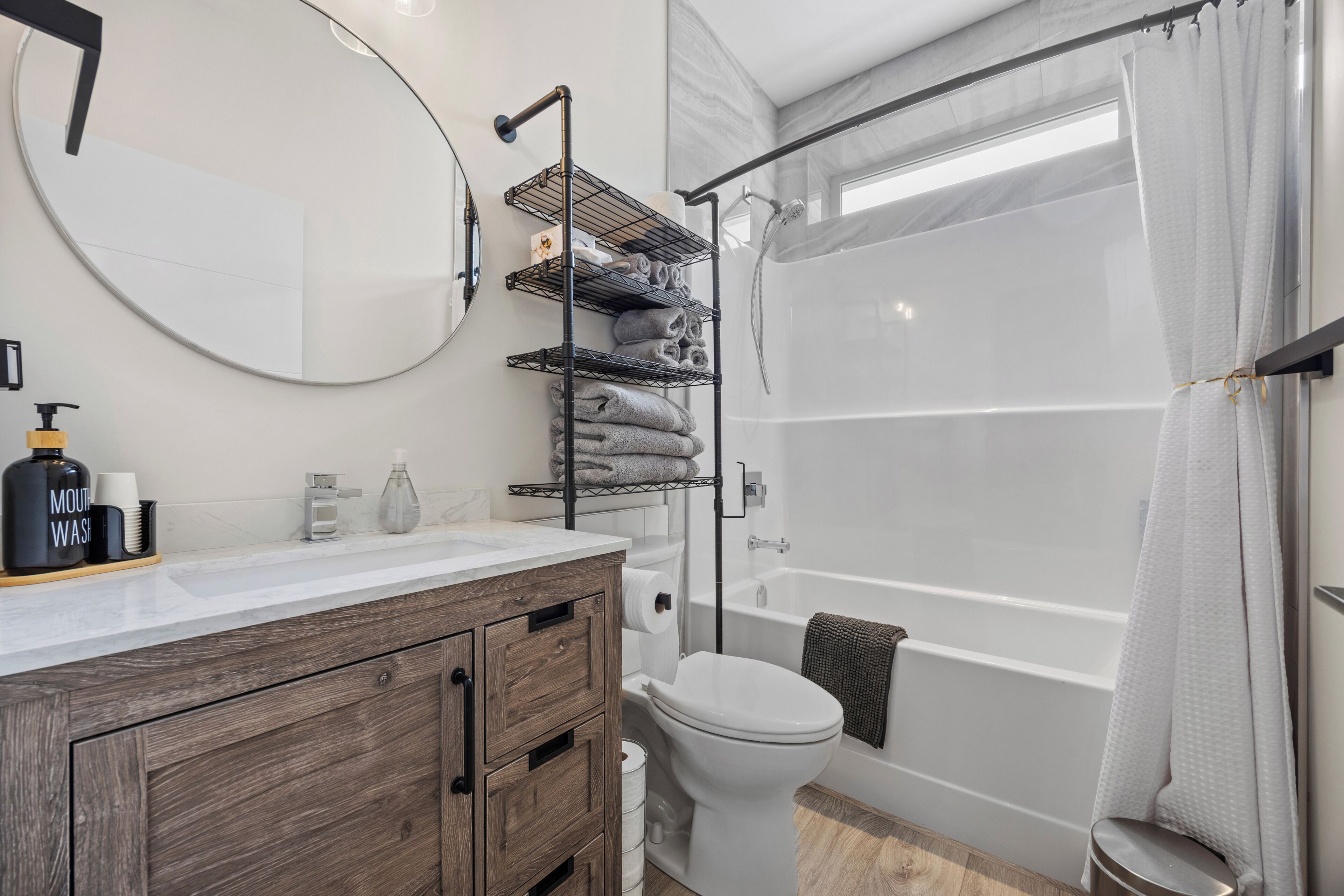 Ein Badezimmer mit Toilette, Holzwaschtisch, Spiegel, Dusche und Badewanne.