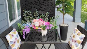 A patio with a glass table, two chairs, a decorative panel, and potted plants.