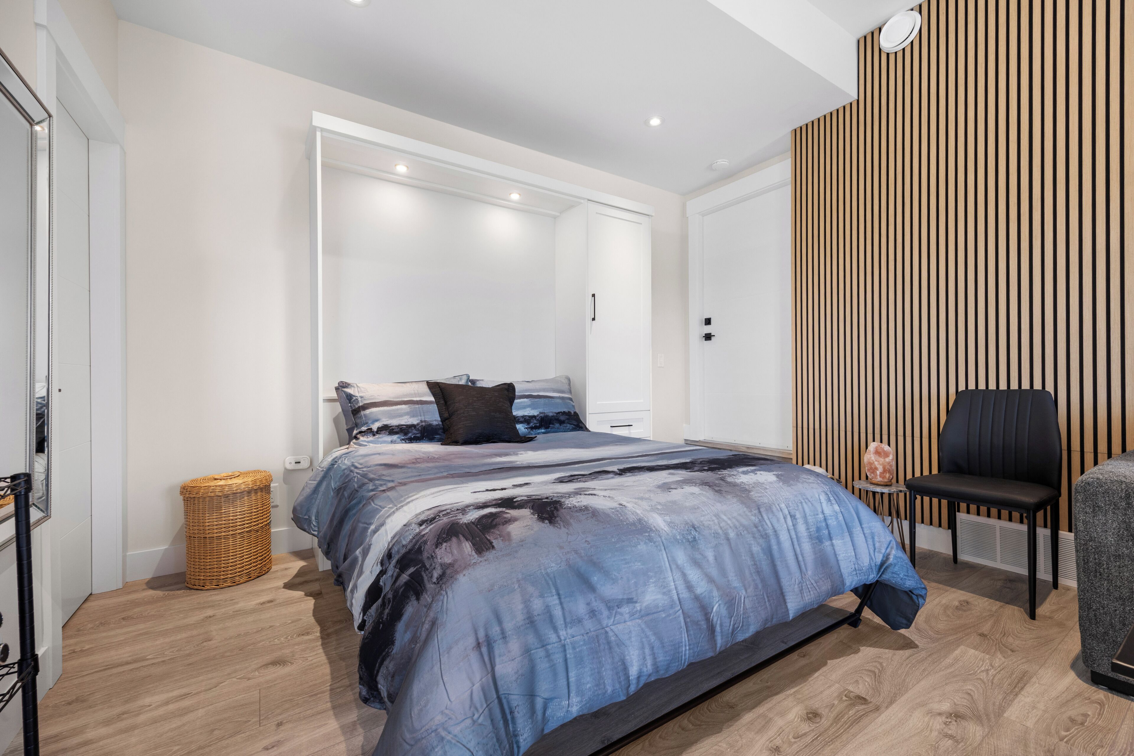 A bedroom with a bed, a chair, a small table, and a wall-mounted heater.