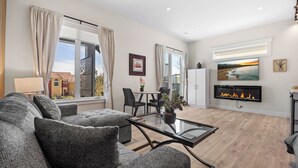 A modern living room with a sofa, a glass coffee table, a fireplace, and a dining area with chairs and a table.