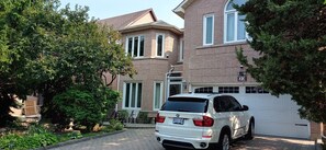 A white car parked in front of a brick house with a garage.