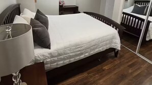A bedroom with a bed, bedside table, lamp, dresser, and a mirror.