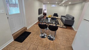 A modern living room with a dining area, grey sofa, and a TV mounted on the wall.