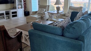 A living room with a teal sofa, a television, and a ceiling fan. - Beachfront Escape – Beach Views from Wraparound Porch•Private Walkover W Seating (Freeport)