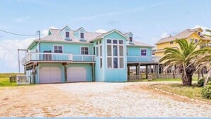 A two-story house with a balcony, a garage, and a sandy driveway. - Beachfront Escape – Beach Views from Wraparound Porch•Private Walkover W Seating (Freeport)