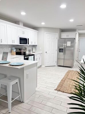A modern kitchen with white cabinets, a stainless steel refrigerator, and a central island with stools.