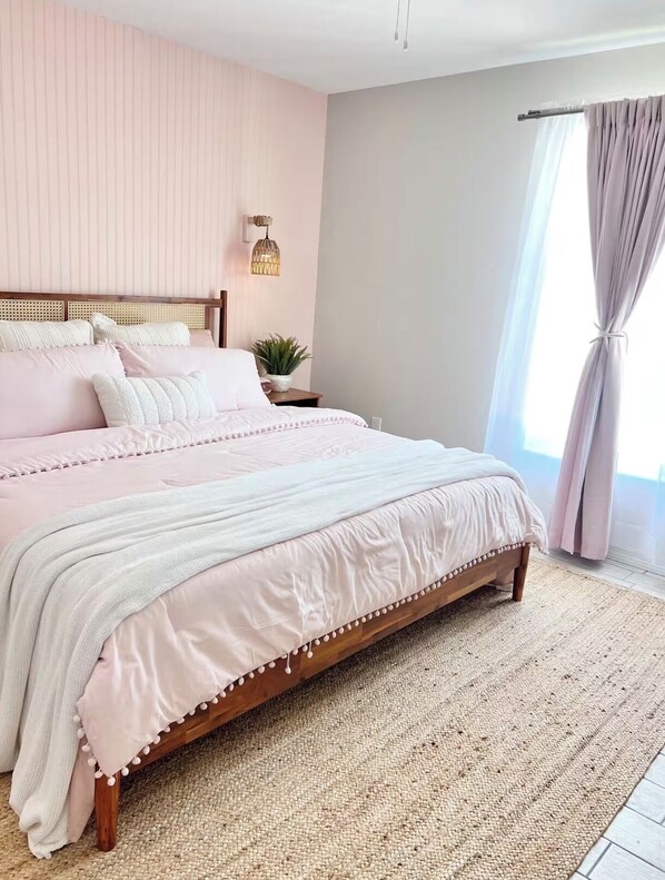 A bedroom with a bed, a nightstand, a wall-mounted lamp, and a window with curtains.