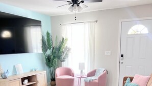 Un salon équipé d’un téléviseur à écran plat, d’un ventilateur de plafond, d’un canapé, de deux fauteuils, d’une petite table et d’une plante en pot.