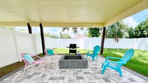 Un patio couvert avec un foyer, des chaises d’extérieur et un barbecue.