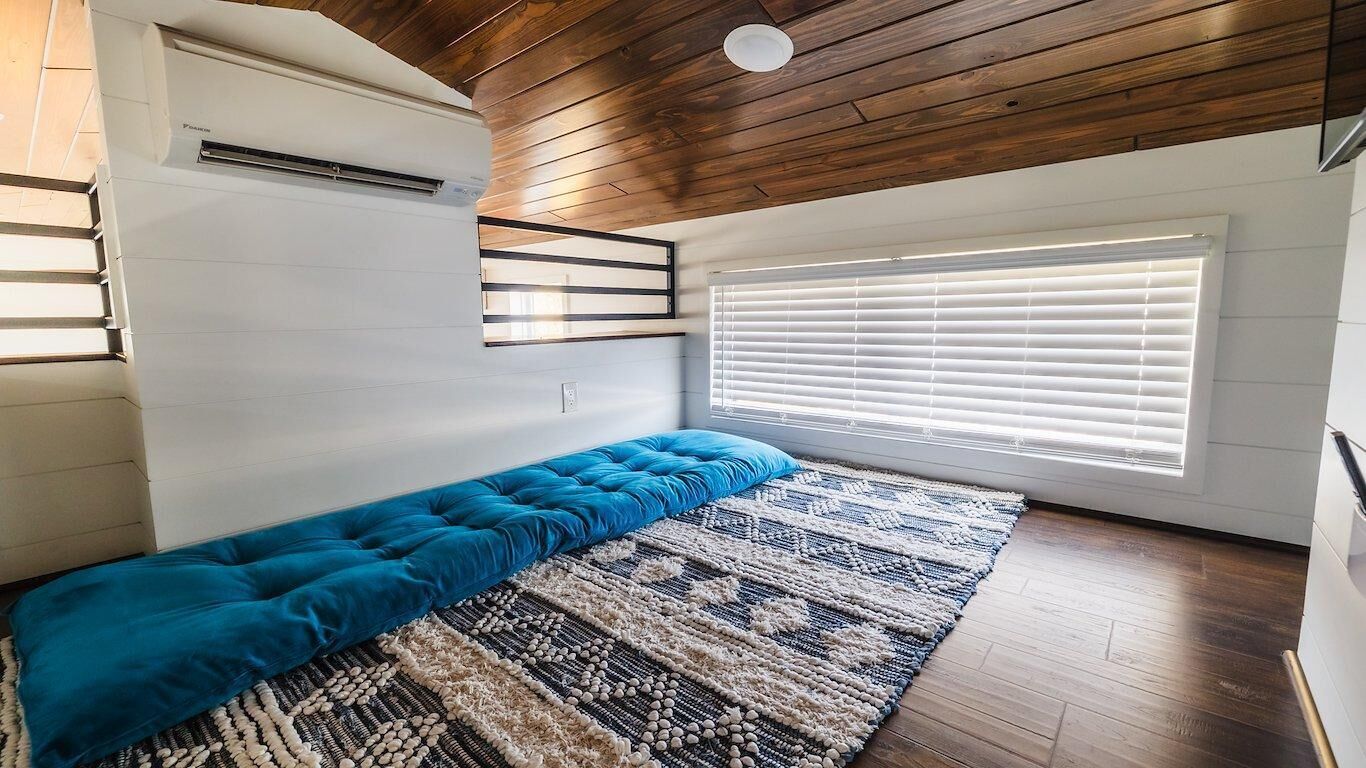 A room with a built-in bench, a large window with blinds, a ceiling fan, and a wall-mounted air conditioning unit.