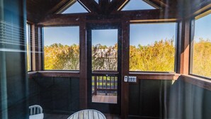 Une pièce avec vue sur les arbres, grâce à de grandes fenêtres, une porte en bois et une petite table.