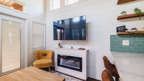 A modern living room with a TV, fireplace, wooden furniture, and a tiled backsplash.