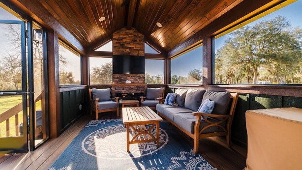 Un espace extérieur aménagé, abrité et doté d’une cheminée en pierre, de mobilier en bois et de grandes fenêtres.