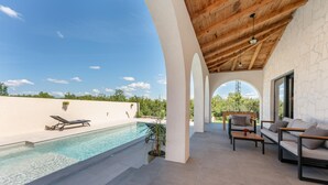 Area piscina con vista aperta sul cielo, una sedia a sdraio, un divano e una pianta in vaso.